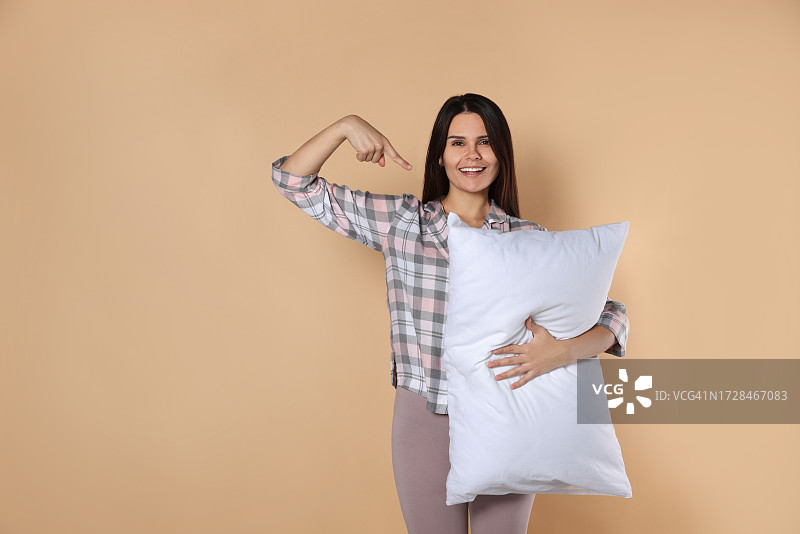 快乐的年轻女人指向米色背景上的柔软枕头，留有文字空间图片素材