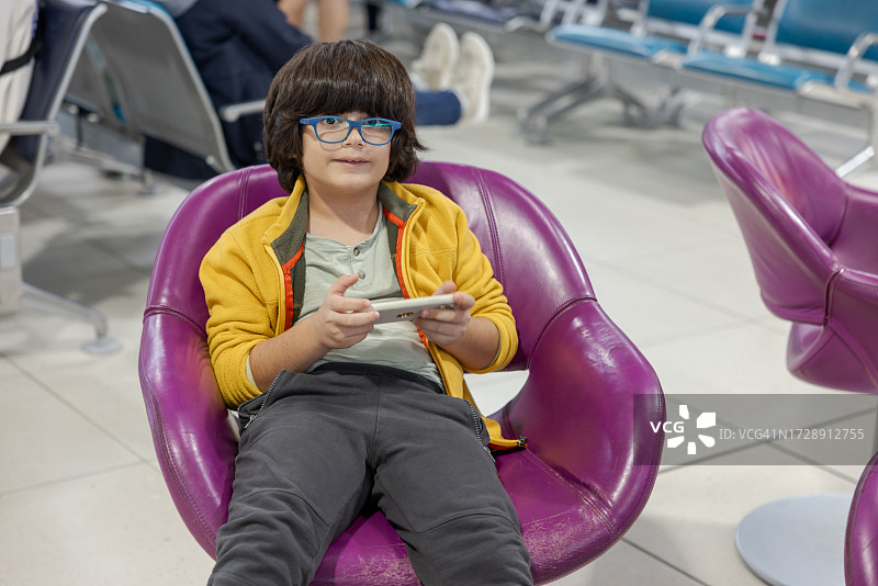 在巴黎戴高乐机场交通区域使用智能手机的8岁混血男孩图片素材