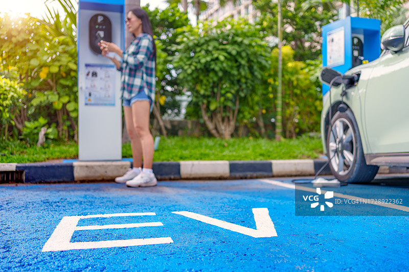 女人在充电站打开插座盖，为电动汽车插入充电器图片素材