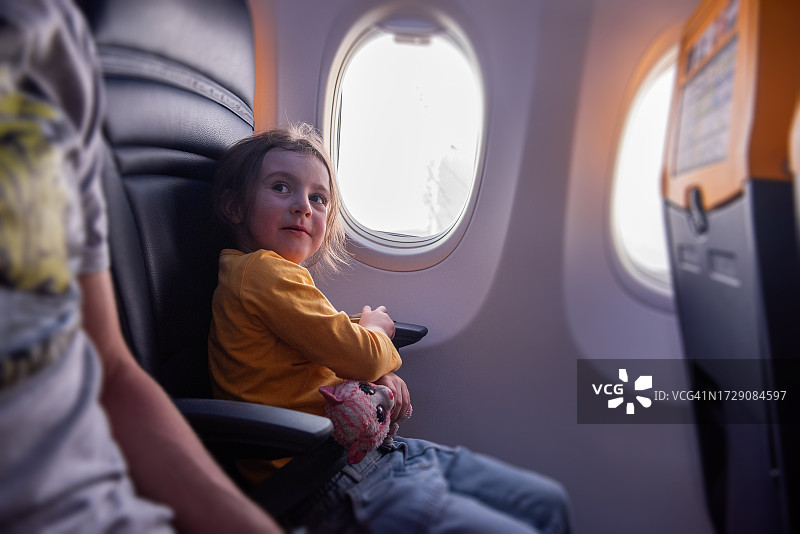 穿着黄色运动衫的小女孩用安全带将毛绒玩具猫固定在飞机上图片素材