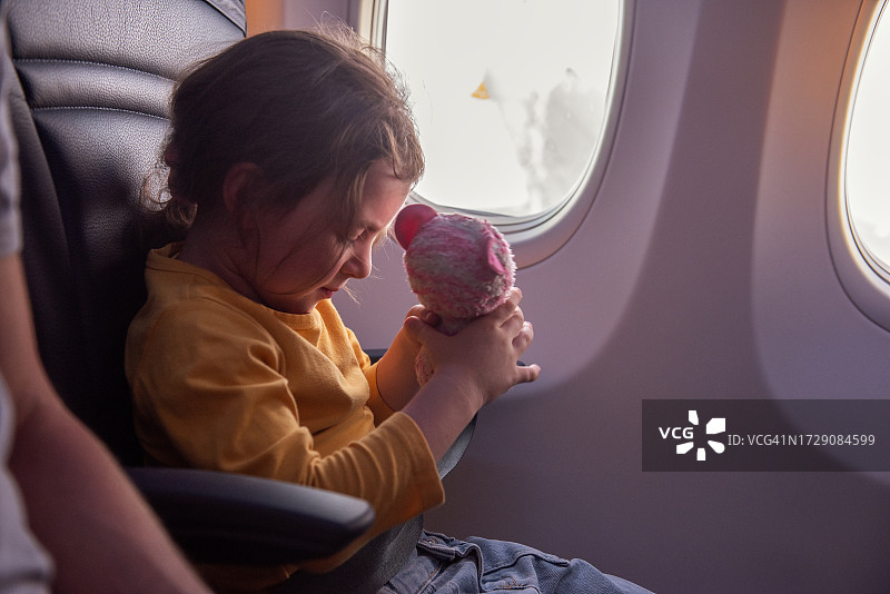 穿着黄色运动衫的小女孩用安全带将毛绒玩具猫固定在飞机上图片素材