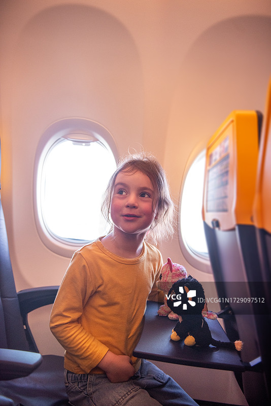 穿着黄色运动衫的小女孩在飞机舷窗旁玩毛绒玩具猫图片素材
