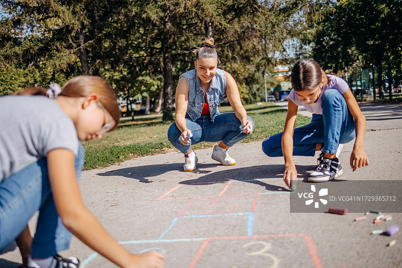 女孩们在公园里用粉笔画画和玩跳房子图片素材