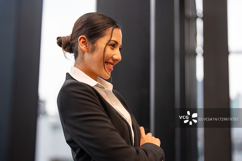 在金融区，一位自信的年轻女商人拿着智能手机站在商业大厦前图片素材