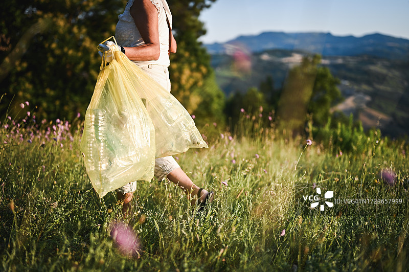 在草地上行走并拿着垃圾袋的女人侧视图图片素材