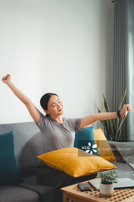 在客厅沙发上放松伸展呼吸新鲜空气的亚洲女人图片素材