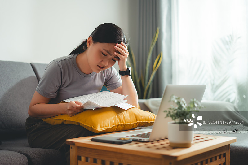 为账单发愁的亚洲女人坐在沙发上图片素材
