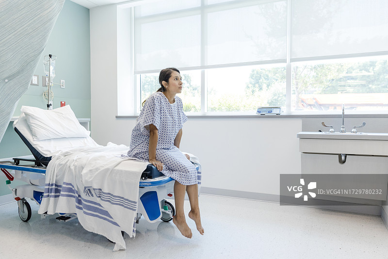 穿着医院病号服的女病人坐在轮床边上图片素材