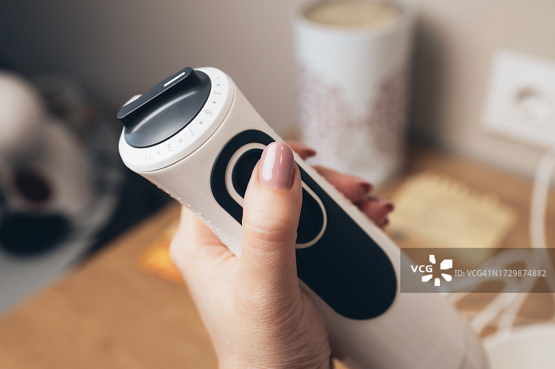 女人按下现代手持搅拌机的按钮图片素材