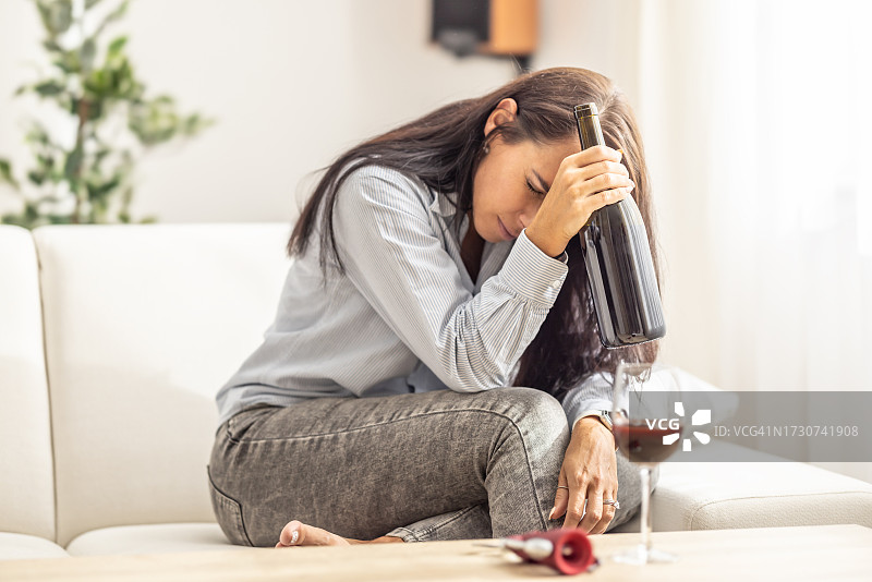 不开心的女人拿着酒瓶坐在沙发上图片素材