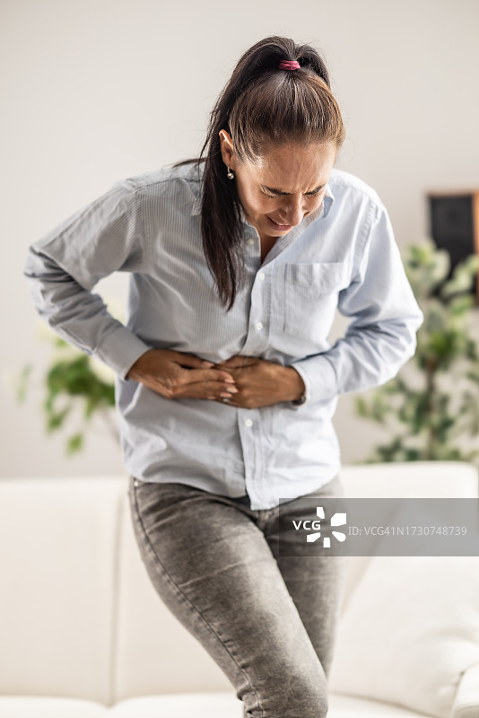 女性因胆囊炎发作而痛苦地蹲伏捂住肚子图片素材