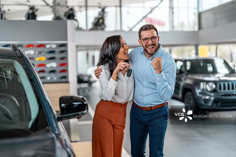 在汽车经销店高兴地拿着新车钥匙的夫妇图片素材
