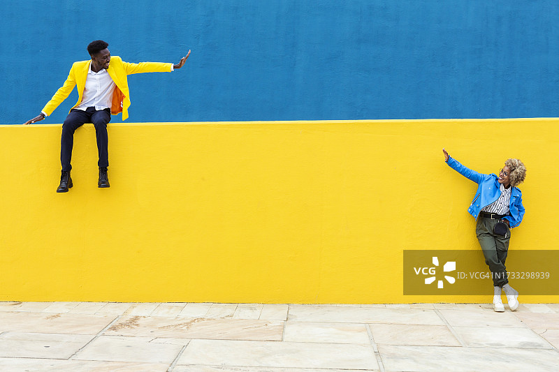 在黄色和蓝色背景下，两位年轻的非洲朋友从远处互相问候。友谊和社交关系概念。有文字的复制空间。图片素材