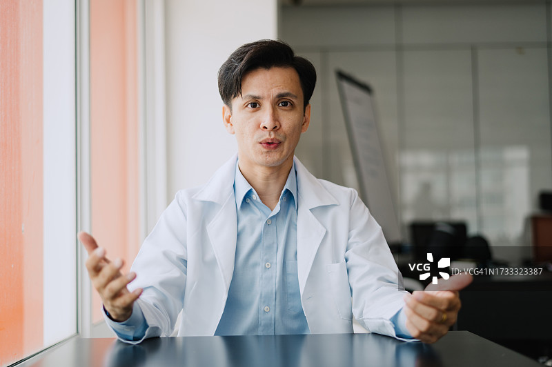 年轻的亚裔中国男医生在网上会议期间对着笔记本电脑讲话的照片图片素材