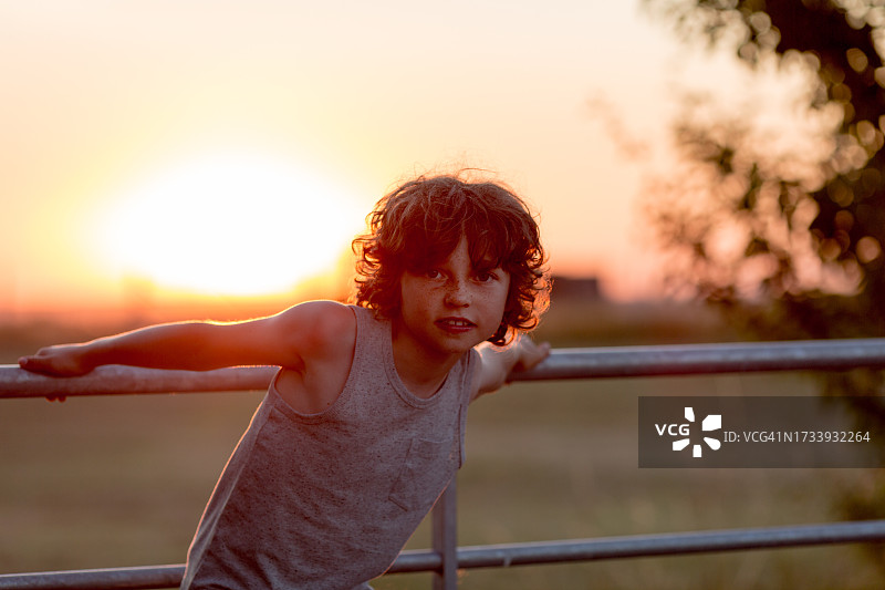 男孩站在日落时分的栅栏上保持平衡图片素材