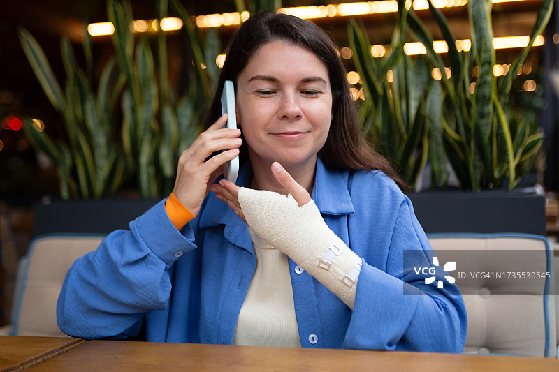 手缠着弹性绷带，在智能手机上交谈的微笑女人图片素材
