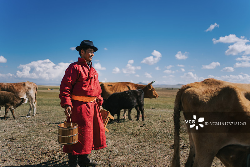 站在牧场上手提牛奶桶眺望远方的蒙古族男人图片素材
