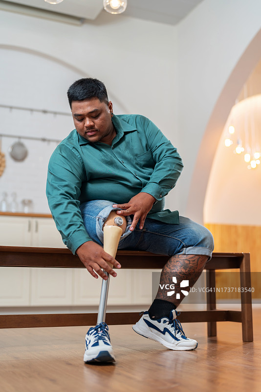 车祸中失去一条腿的男人坐在椅子上，若有所思地看着假肢图片素材