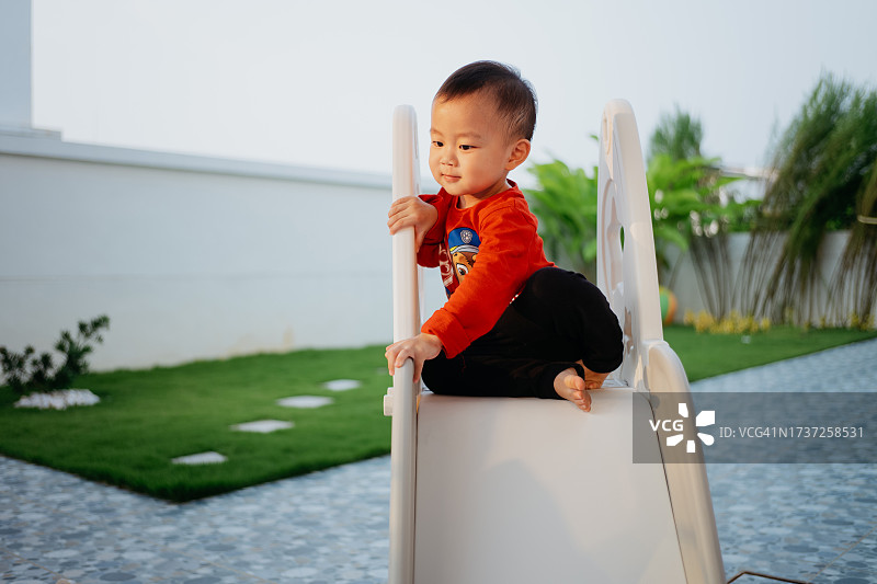 在后院滑梯上休息的亚洲幼儿男孩图片素材