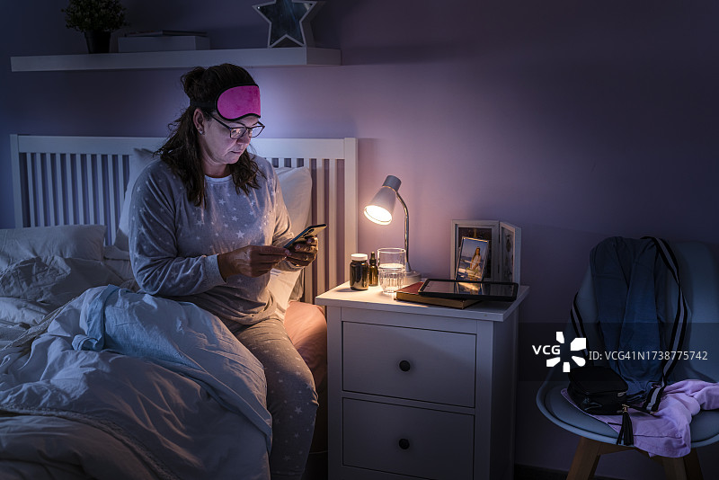失眠的女人坐在床上查看手机图片素材