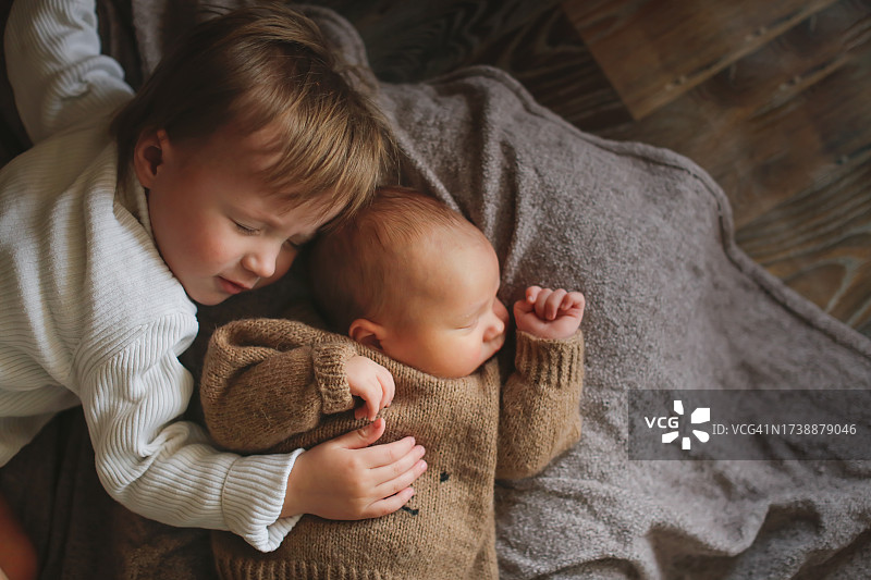 充满爱意的兄妹情：俯视照片中，姐姐拥抱着穿着针织羊毛套装的弟弟，棕色格子背景，留有文案空间图片素材