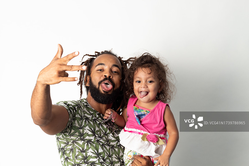 留着脏辫的拉丁裔父亲抱着女儿，高兴地对着镜头吐舌头图片素材