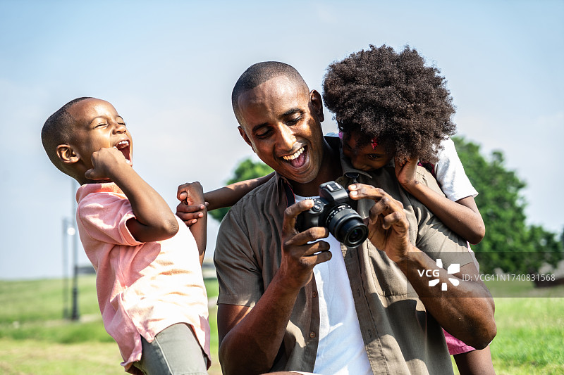 父亲在公园里向孩子们展示数码相机里的照片图片素材