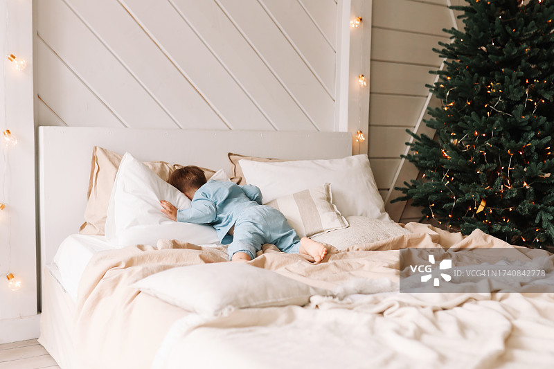 一个悲伤孤独的小男孩在装饰过的圣诞树旁的床上对着枕头哭喊图片素材
