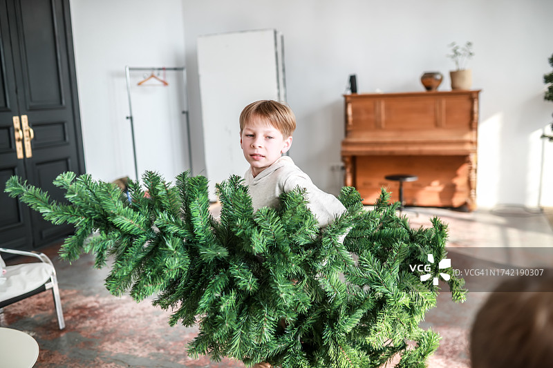 有趣的圣诞节准备：金发男孩抱着圣诞树奔跑图片素材