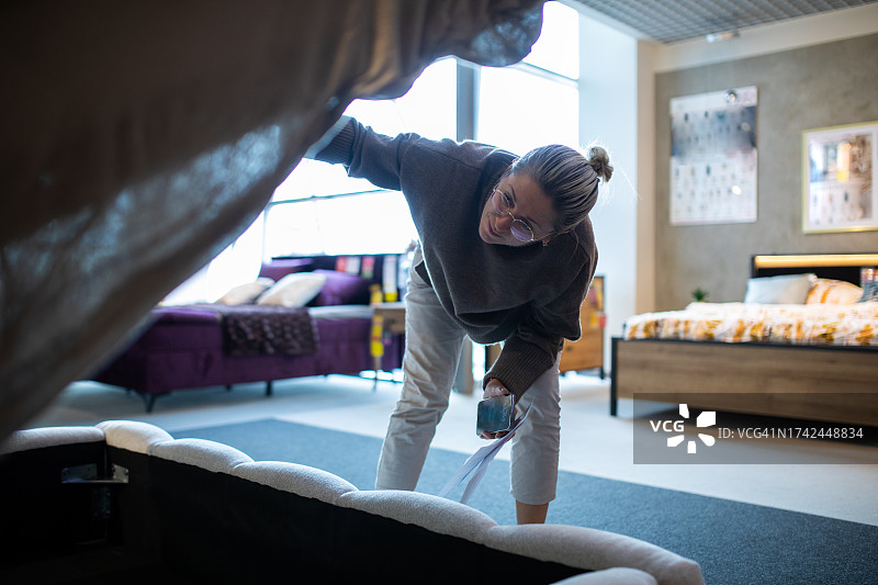 迷人的女人专心研究商店里的床，抬起床垫，露出下面隐藏的存储空间图片素材