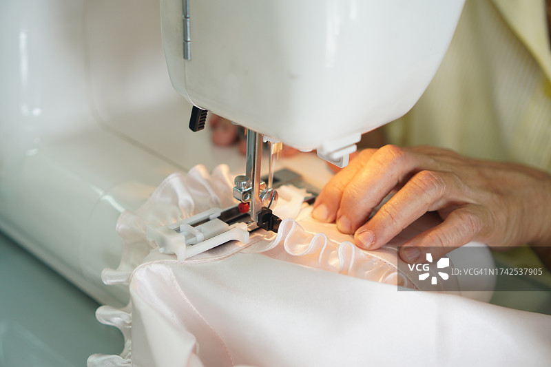缝纫机特写：女士使用缝纫机缝制白色缎面连衣裙图片素材
