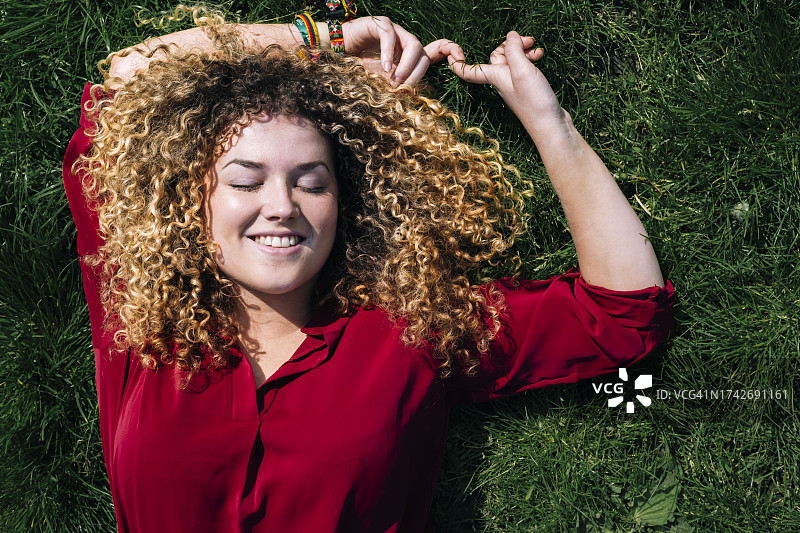 在草地上微笑的卷发女人图片素材