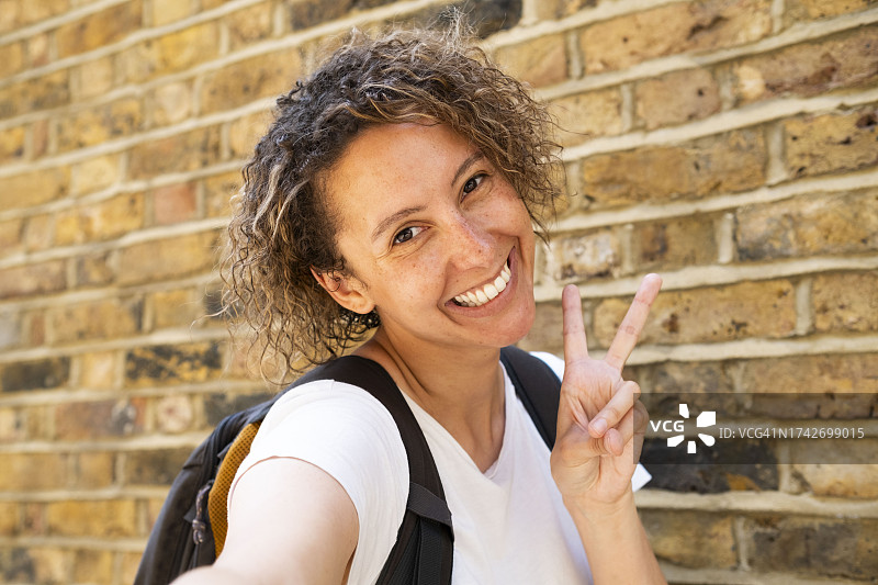 在砖墙前做出和平手势的快乐女商人图片素材