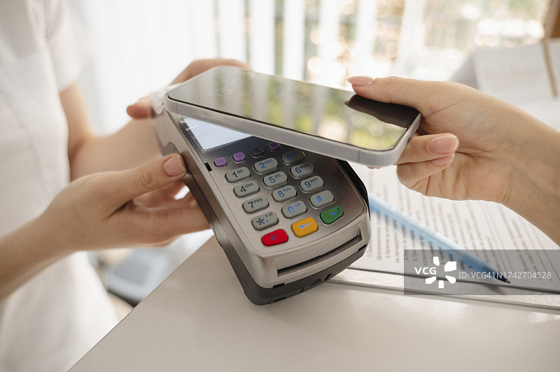女人在诊所通过智能手机在信用卡读卡器上支付图片素材