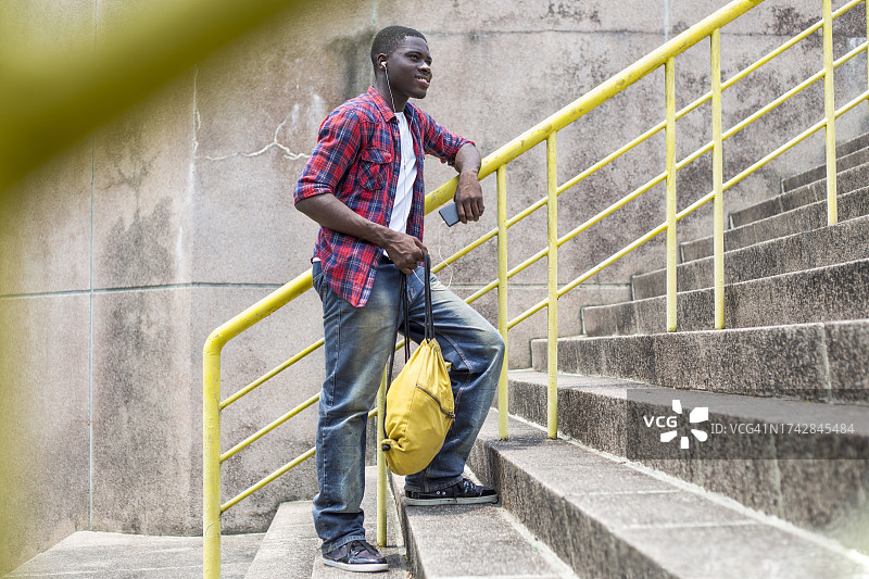 快乐的年轻人听着音乐，靠在栏杆上玩手机图片素材