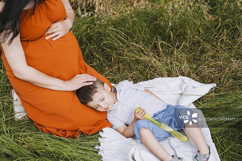 怀孕的母亲抚摸着在草地上睡觉的儿子图片素材