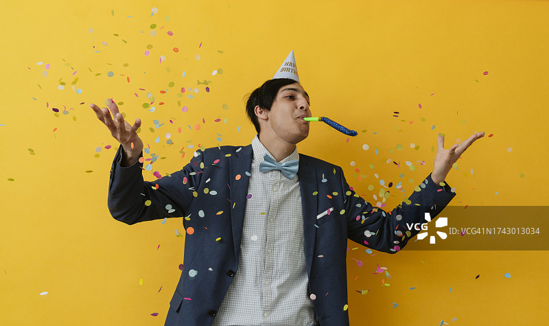 年轻男子在演播室吹响派对喇叭并抛洒五彩纸屑图片素材