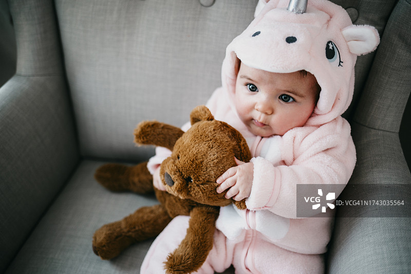 打扮成独角兽的女婴抱着她的泰迪熊图片素材