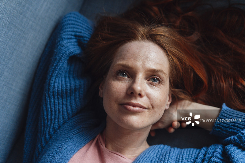 微笑的红发女子在沙发上放松图片素材