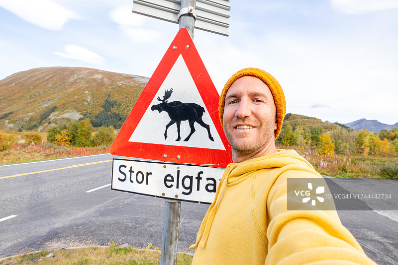 男子与驼鹿出没警告牌的趣味自拍图片素材