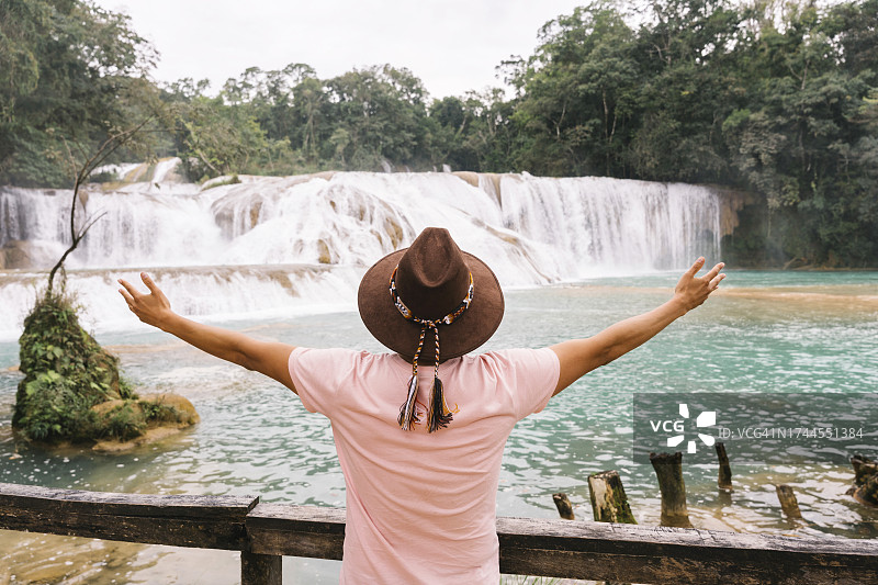 在蓝色瀑布和树木前伸开双臂的男人图片素材