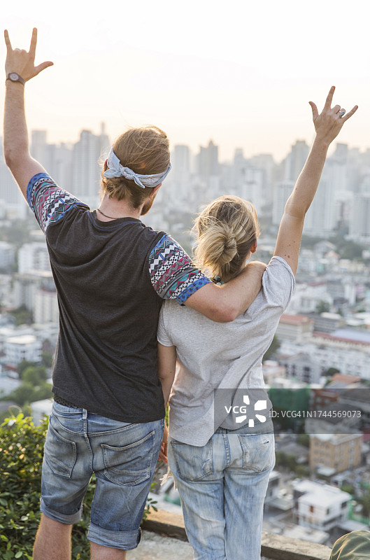 情侣在日落时分在城市景观前做出摇滚手势图片素材
