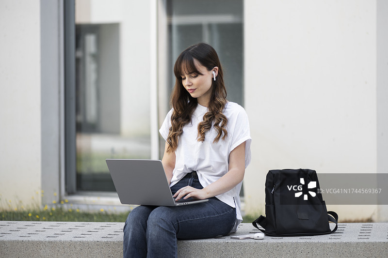 年轻女人在建筑物前使用笔记本电脑图片素材