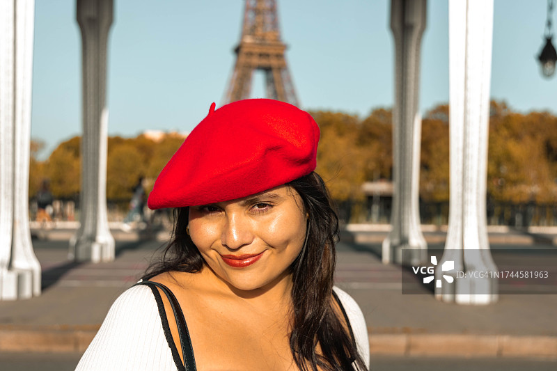 戴红色贝雷帽的拉丁裔女子在埃菲尔铁塔前的肖像图片素材