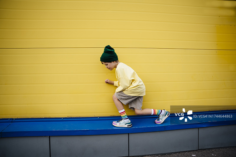 穿着运动衫蹲在黄色墙前的顽皮男孩图片素材