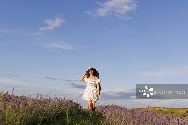 身穿白色连衣裙的女人在阳光明媚的日子里在田野里行走图片素材
