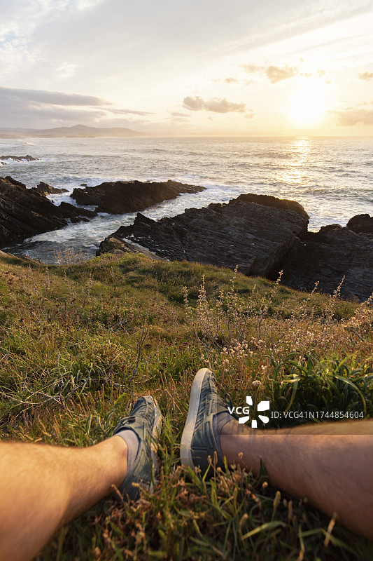男人坐在海边草地上看日落图片素材