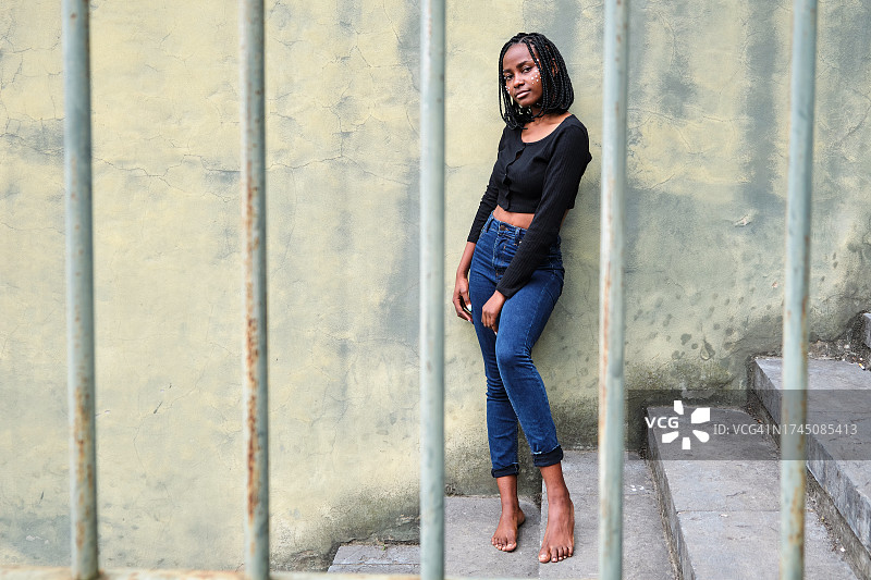 编着辫子、戴着珍珠的非洲妇女站在楼梯上，透过金属栏杆向外看图片素材