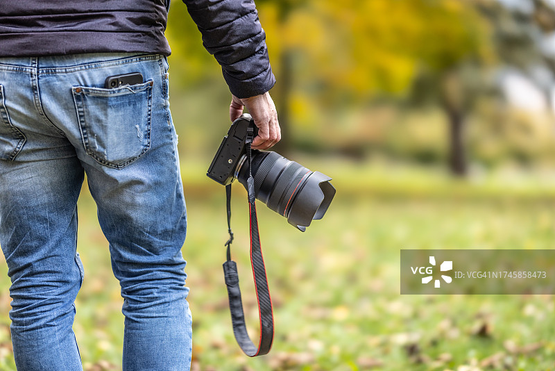在秋日公园某处拿着相机的男人的背影图片素材