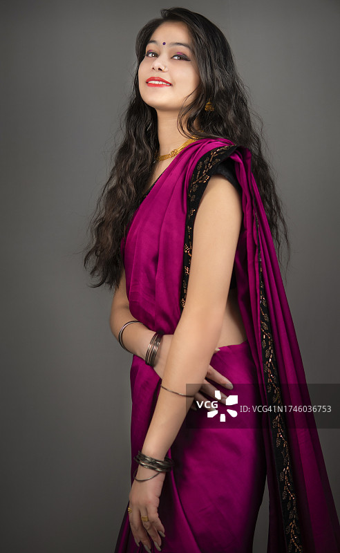 快乐的印度年轻女子穿着纱丽和金色珠宝看着镜头的肖像图片素材